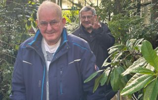 Botanischer Garten Marburg Senior mit Rollator lächelt zwischen grünen Pflanzen im Gewächshaus