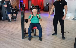 Regelmäßige Besuche im Fitnessstudio Seniorin trainiert an einem Gerät, ein Trainer schaut zu