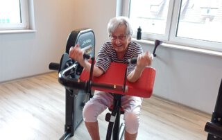Regelmäßige Besuche im Fitnessstudio Seniorin trainiert an einem roten Trainingsgerät am Fenster