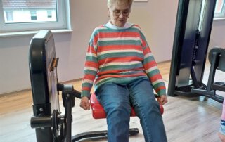 Regelmäßige Besuche im Fitnessstudio Seniorin im gestreiften Pullover trainiert an der Beinstreckmaschine