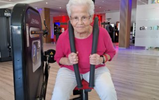 Regelmäßige Besuche im Fitnessstudio Seniorin im pinken Pullover an einem Kraftgerät