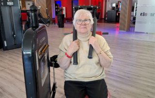 Regelmäßige Besuche im Fitnessstudio Seniorin trainiert an einem Kraftgerät mit Schulterpolstern