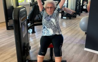 Regelmäßige Besuche im Fitnessstudio Seniorin hebt beim Training beide Arme