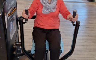 Regelmäßige Besuche im Fitnessstudio Seniorin trainiert lachend an der Brustpresse