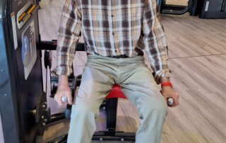 Regelmäßige Besuche im Fitnessstudio Senior im karierten Hemd an einem Kraftgerät