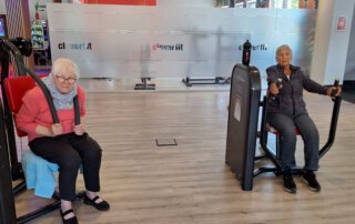 Regelmäßige Besuche im Fitnessstudio Zwei Seniorinnen trainieren an gegenüberliegenden Geräten