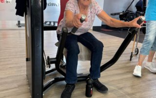 Regelmäßige Besuche im Fitnessstudio Seniorin trainiert die Arme an einem Zuggerät