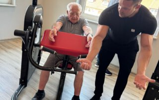 Regelmäßige Besuche im Fitnessstudio Trainer zeigt einem Senior eine Übung am Gerät