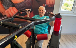 Regelmäßige Besuche im Fitnessstudio Seniorin trainiert an einem Rudergerät vor einem großen Wandbild