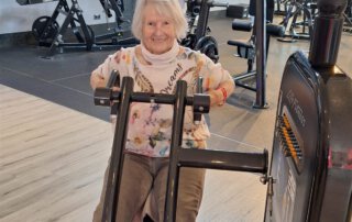 Regelmäßige Besuche im Fitnessstudio Seniorin trainiert lächelnd an einem Zuggerät