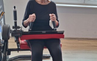 Regelmäßige Besuche im Fitnessstudio Seniorin im schwarzen Oberteil an einem Trainingsgerät