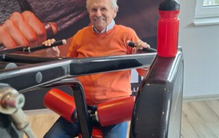 Regelmäßige Besuche im Fitnessstudio Seniorin im orangen Pullover trainiert am Rudergerät