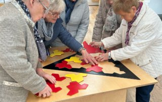 Seniorinnen legen gemeinsam ein Puzzle auf einem dreieckigen Tisch