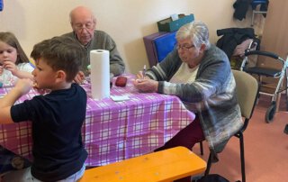 Ostereier färben mit der Kita Regenbogen Junge und Seniorin sitzen im Kindergarten am Basteltisch
