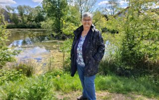 Seniorin steht am Ufer des Teichs in Speckswinkel