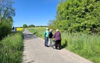 Gäste spazieren auf einem Feldweg in Richtung Teich