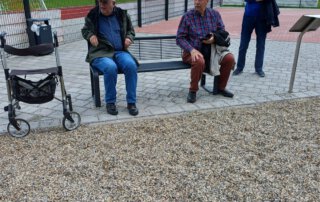 Gäste sitzen auf einer Bank am neuen Sportplatz