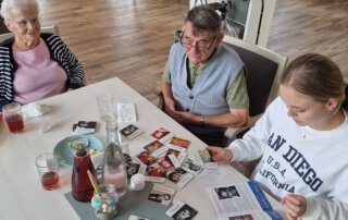 Praktikantin schaut mit Gästen alte Fotos am Tisch an