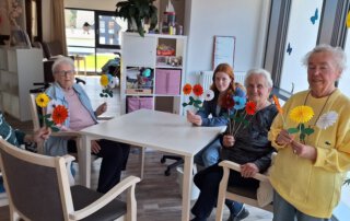 Gäste und Praktikantinnen sitzen mit gelben Blumen am Tisch