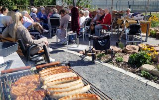 Zwei sommerliche Grillwochen mit fröhlicher Stimmung Grill mit Steaks und Würstchen, im Hintergrund die Gäste unter Sonnenschirmen
