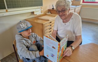 Meet and Read Seniorin liest einem Jungen aus einem Bilderbuch vor